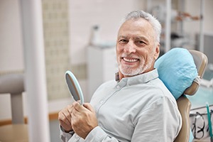 patient smiling while holding dental mirror 