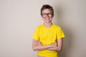 Boy wearing yellow shirt and large eyeglasses smiling with braces.